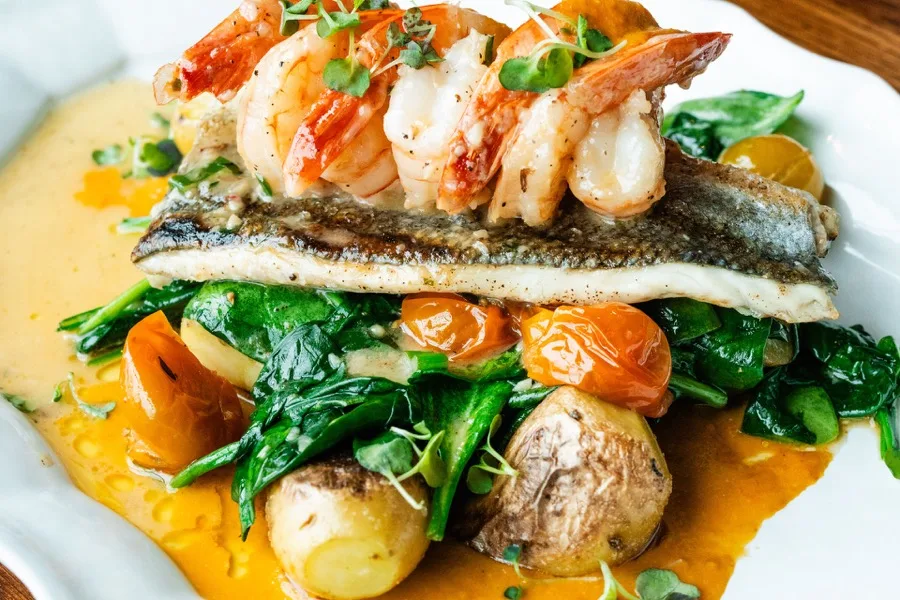 Grilled branzino topped with shrimp over spinach and fingerling potatoes